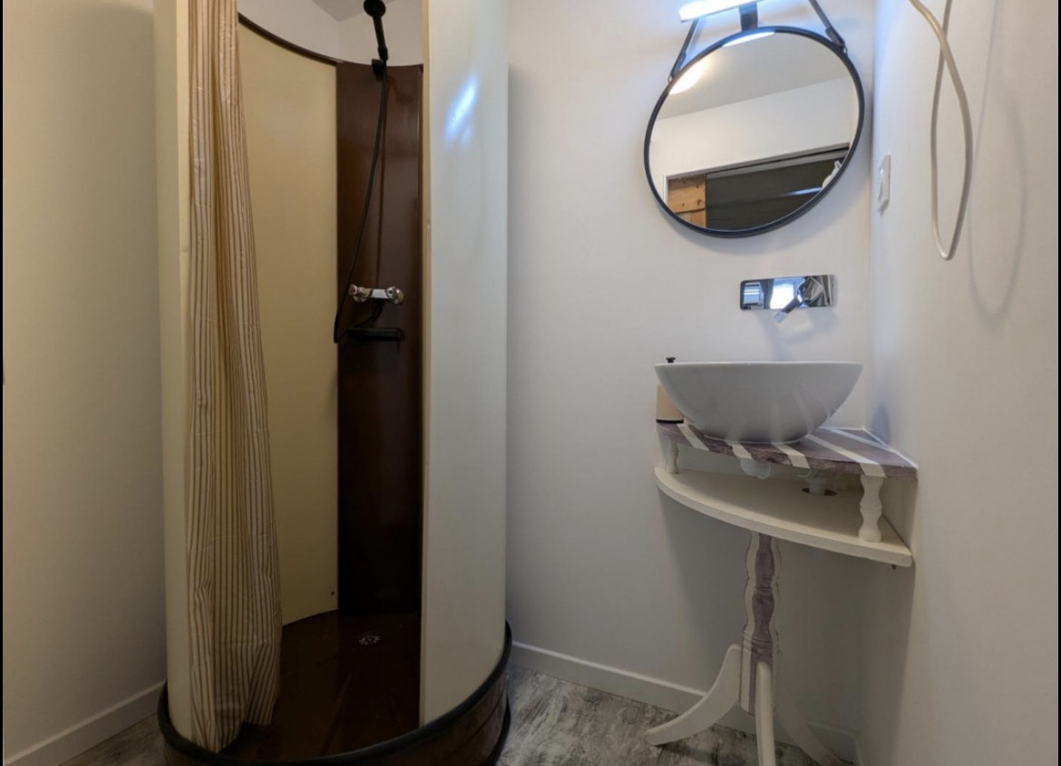 Salle d’eau du rez-de-chaussée de L’Étape Atypique avec douche, lavabo et miroir rond
